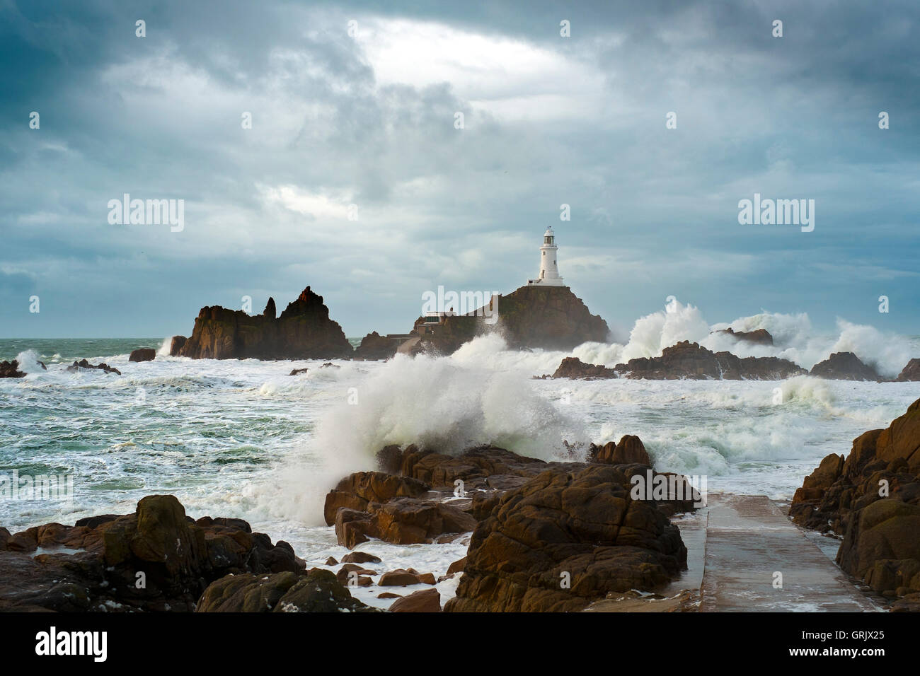 Corbiere lighthouse (Jersey) con alta venti causando enormi ondate di crash sulle rocce della costa frastagliata. Foto Stock