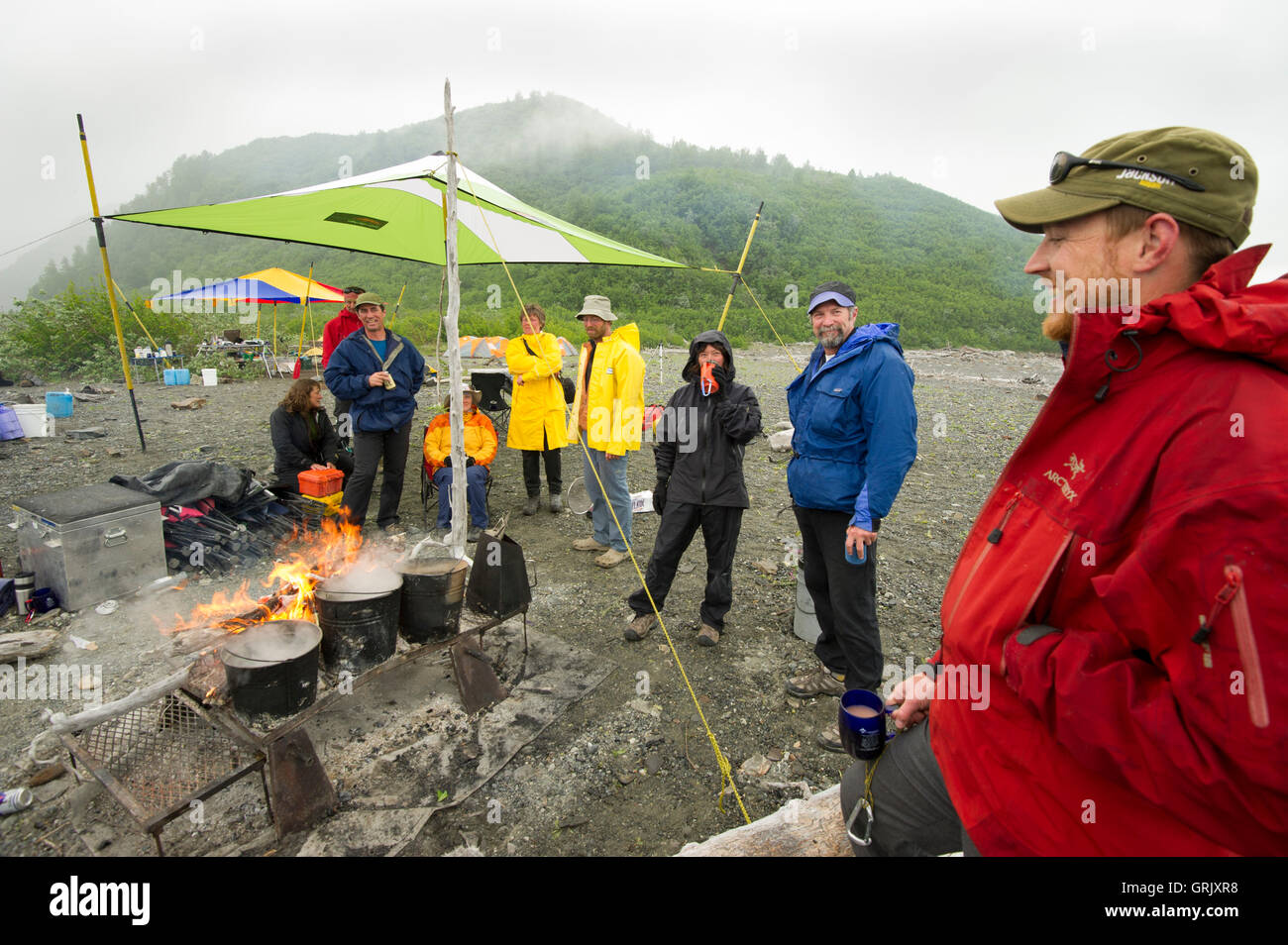 Rafters relax intorno al fuoco in un giorno di pioggia lungo le rive del lago Alsek, Alsek River Foto Stock