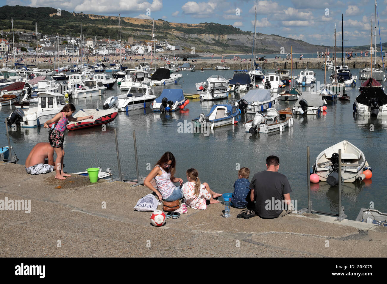 Una famiglia seduta sul molo di Cobb con una vista delle barche nel porto in estate a Lyme Regis DORSET REGNO UNITO Inghilterra KATHY DEWITT Foto Stock