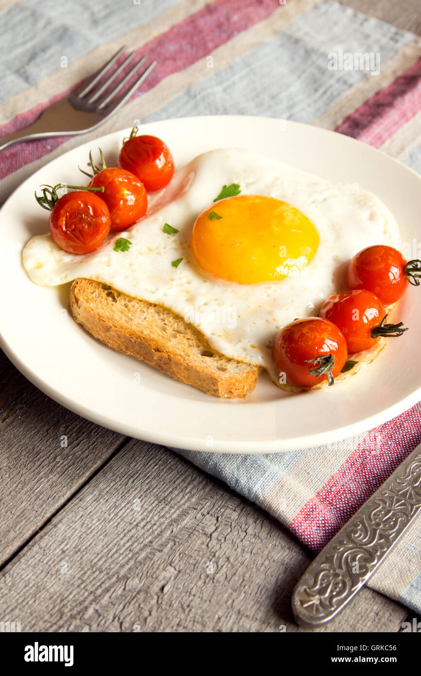 Uovo fritto sul pane e pomodori fritti per la colazione sulla piastra e tavolo rustico Foto Stock