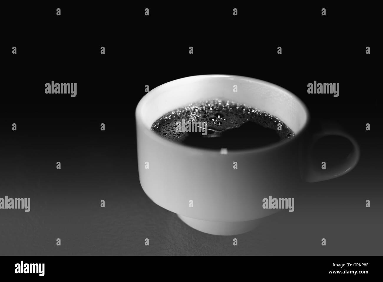 Tazza di caffè su un tavolo di vetro in B&W. White Tazza da caffè Close Up con sfondo scuro e luce drammatica. Foto Stock