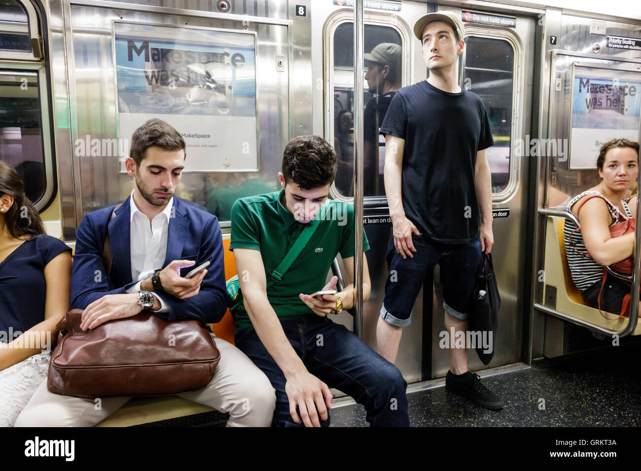 NY NYC,New York City,Manhattan metropolitana MTA treno, uomo uomini maschio cellulare smartphone smartphone,controllare cercando di leggere messaggi SMS passeggeri r Foto Stock