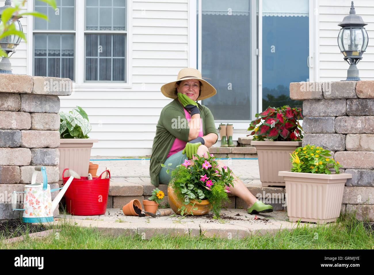 Nonna inglobamento delle piante sul suo patio seduta sul passo di mattone circondato da fresche piantine e vasi da fiori cercando pensiv Foto Stock