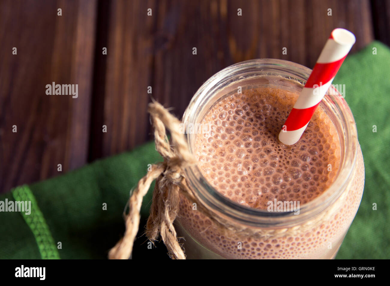 Frullato al cioccolato (frullato) con paglia in barattolo scuro sul tavolo di legno Foto Stock