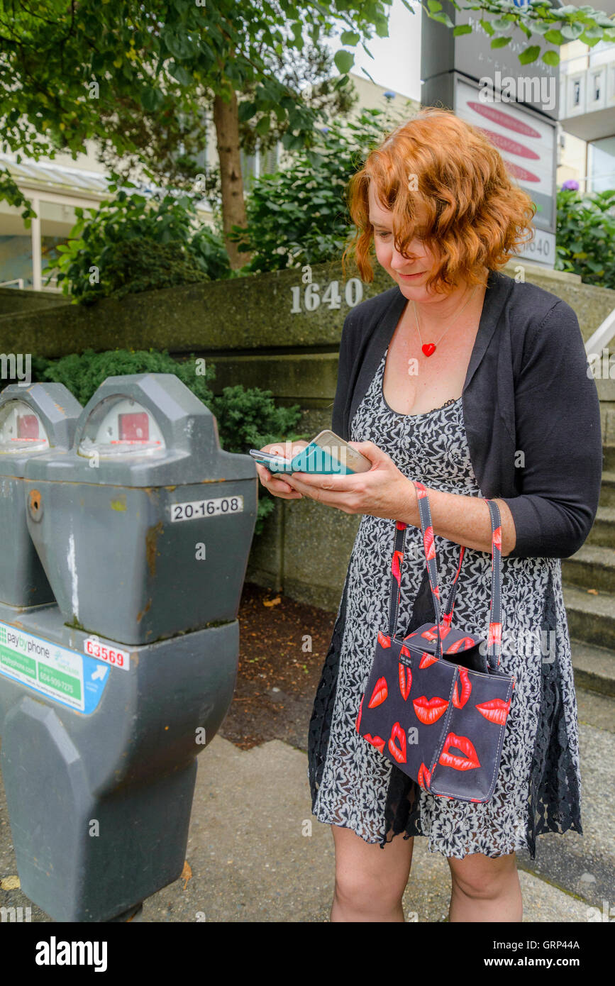 Donna che utilizza il pagamento tramite telefono cellulare smartphone app a pagare per il parcheggio auto, Vancouver, British Columbia, Canada Foto Stock