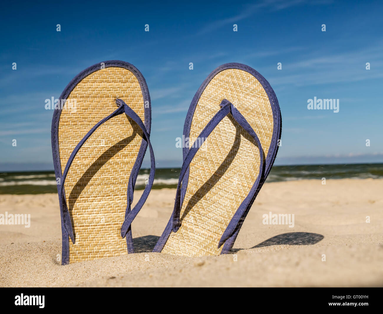 Coppia di paglia flip-flop bloccato in spiaggia di sabbia oltre il cielo blu Foto Stock