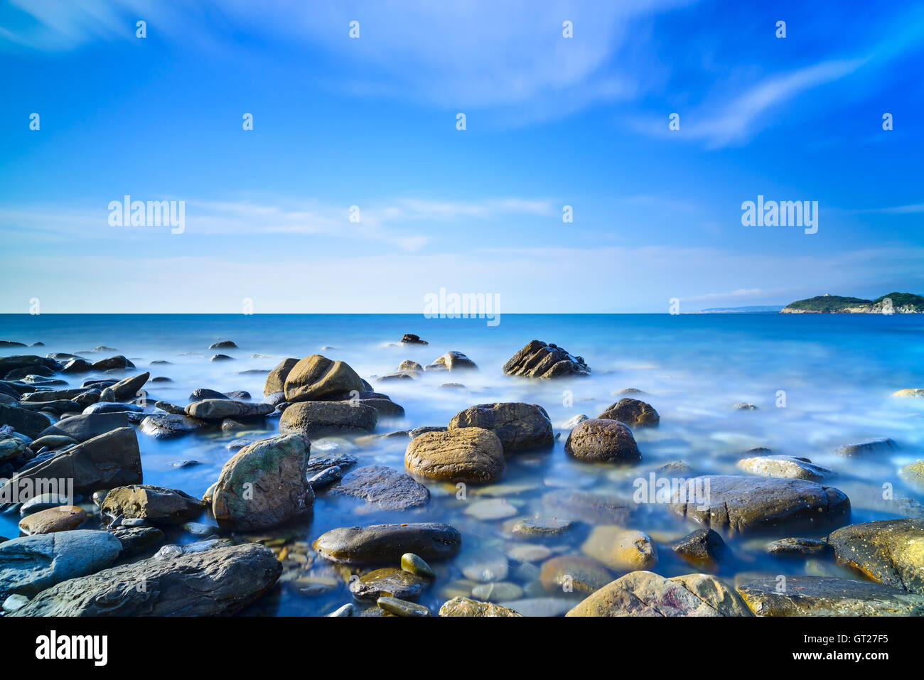 Baratti bay, rocce in un oceano blu sotto un cielo chiaro sul tramonto. Toscana, Italia. Foto Stock