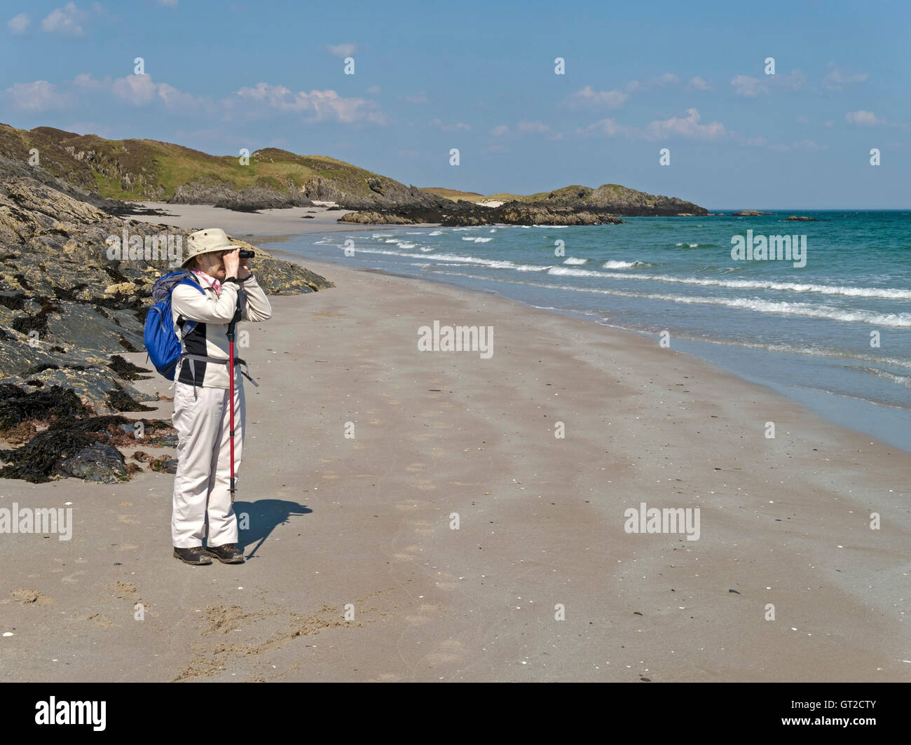 Donna che utilizza un binocolo sulla spiaggia sabbiosa, Isola di Colonsay, Scotland, Regno Unito. Foto Stock