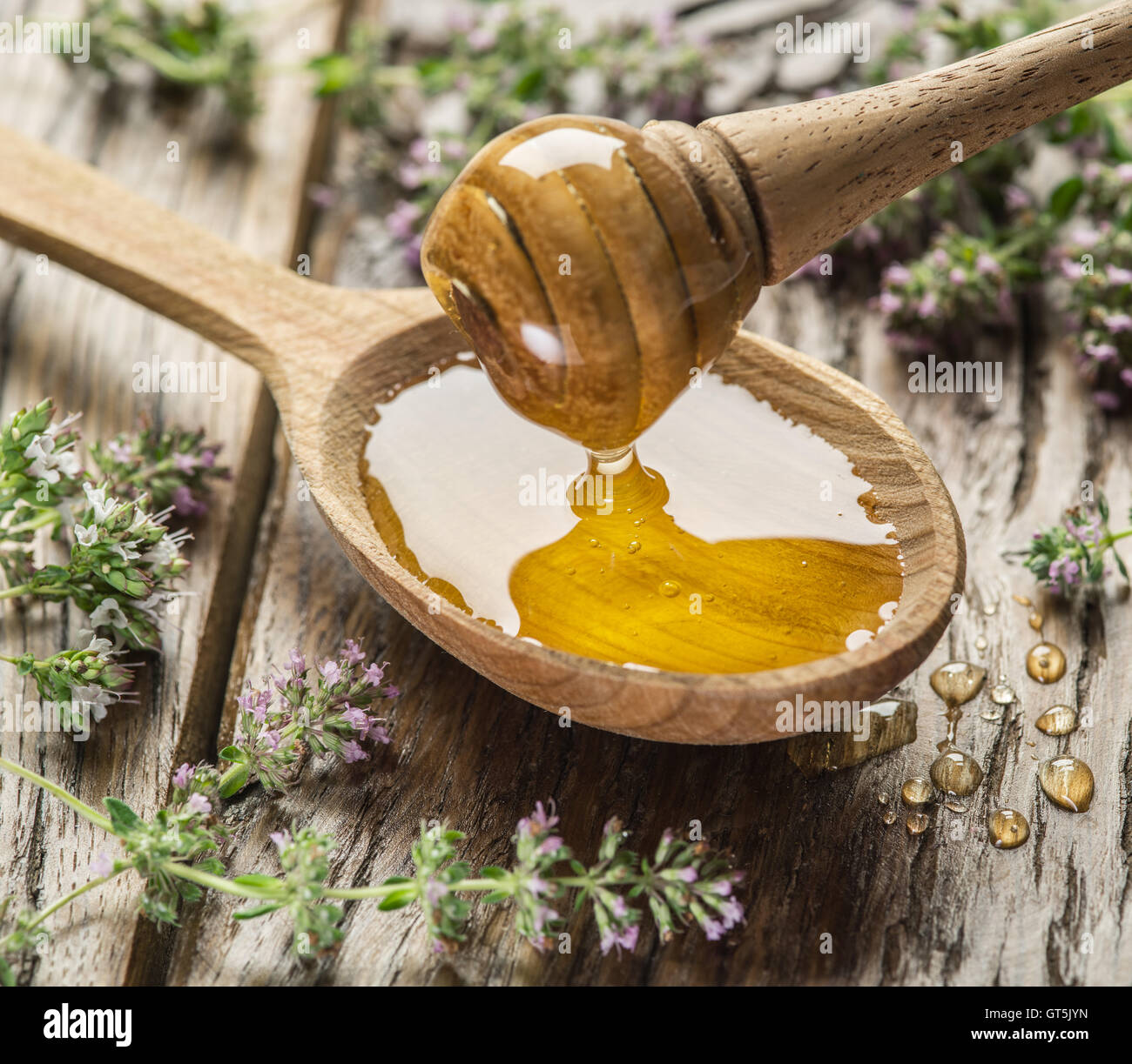 Il miele di erbe versando in il cucchiaio di legno. Cucchiaio è sul vecchio tavolo in legno circondato con fiori di lavanda. Foto Stock