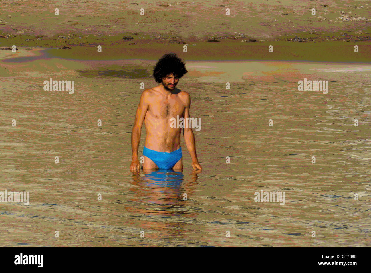 Un giovane uomo di grandi capelli entra in acqua Cefalu, Sicilia Foto Stock