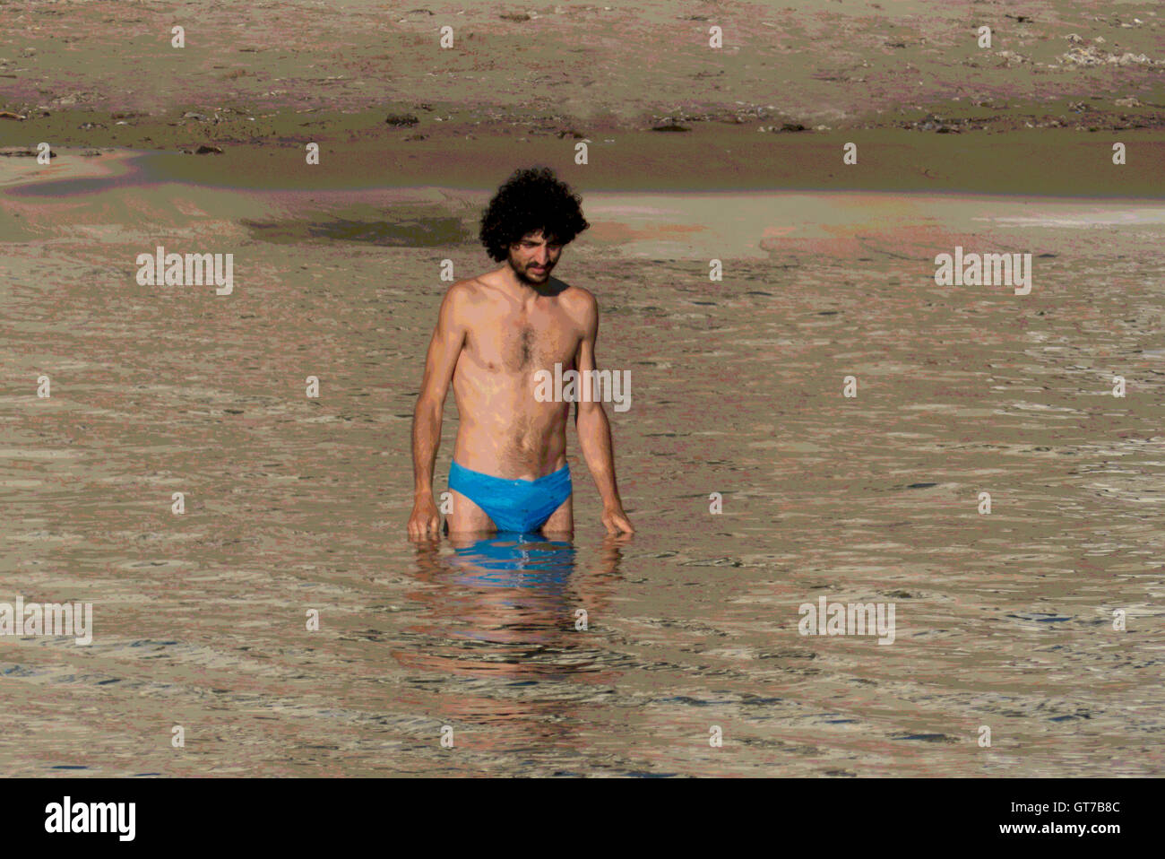 Un giovane uomo di grandi capelli entra in acqua Cefalu, Sicilia Foto Stock