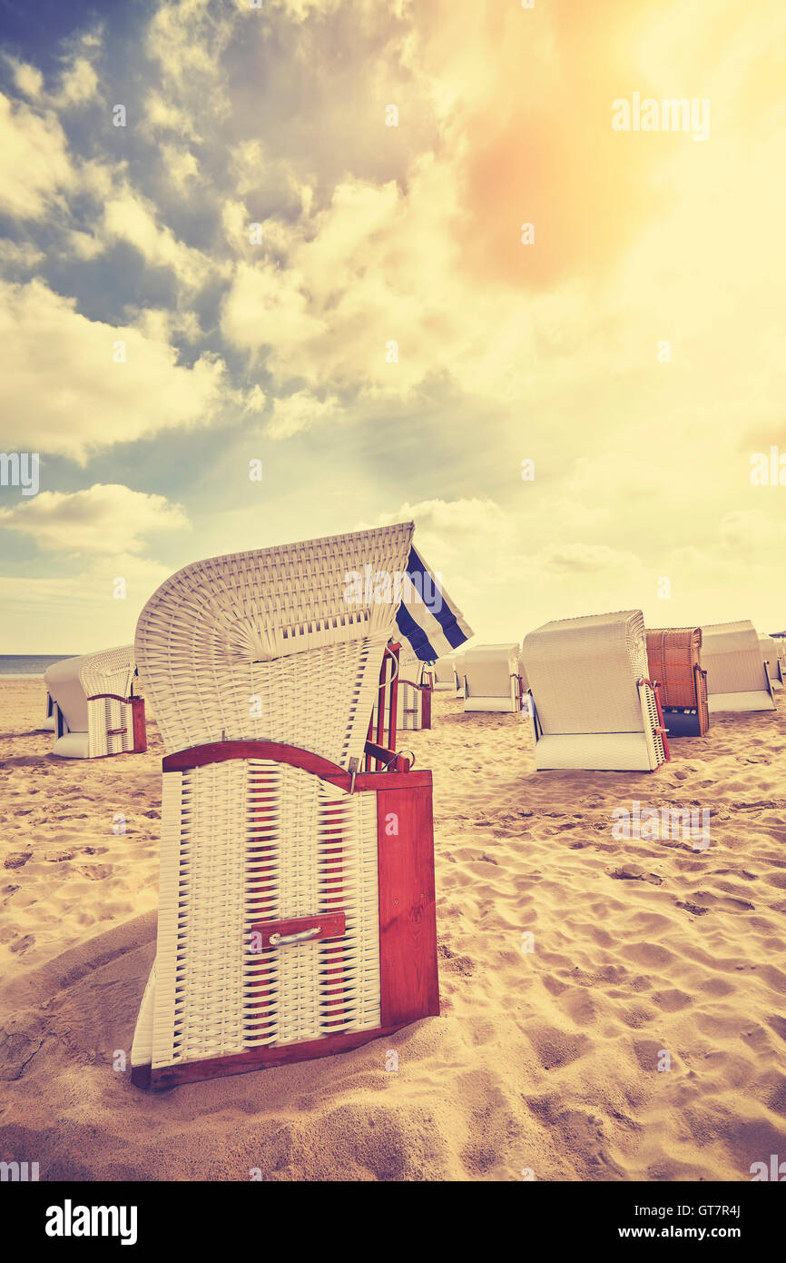 Vintage tonica incappucciati sedie da spiaggia in vimini su una spiaggia deserta al tramonto, vacanze estive concetto. Foto Stock