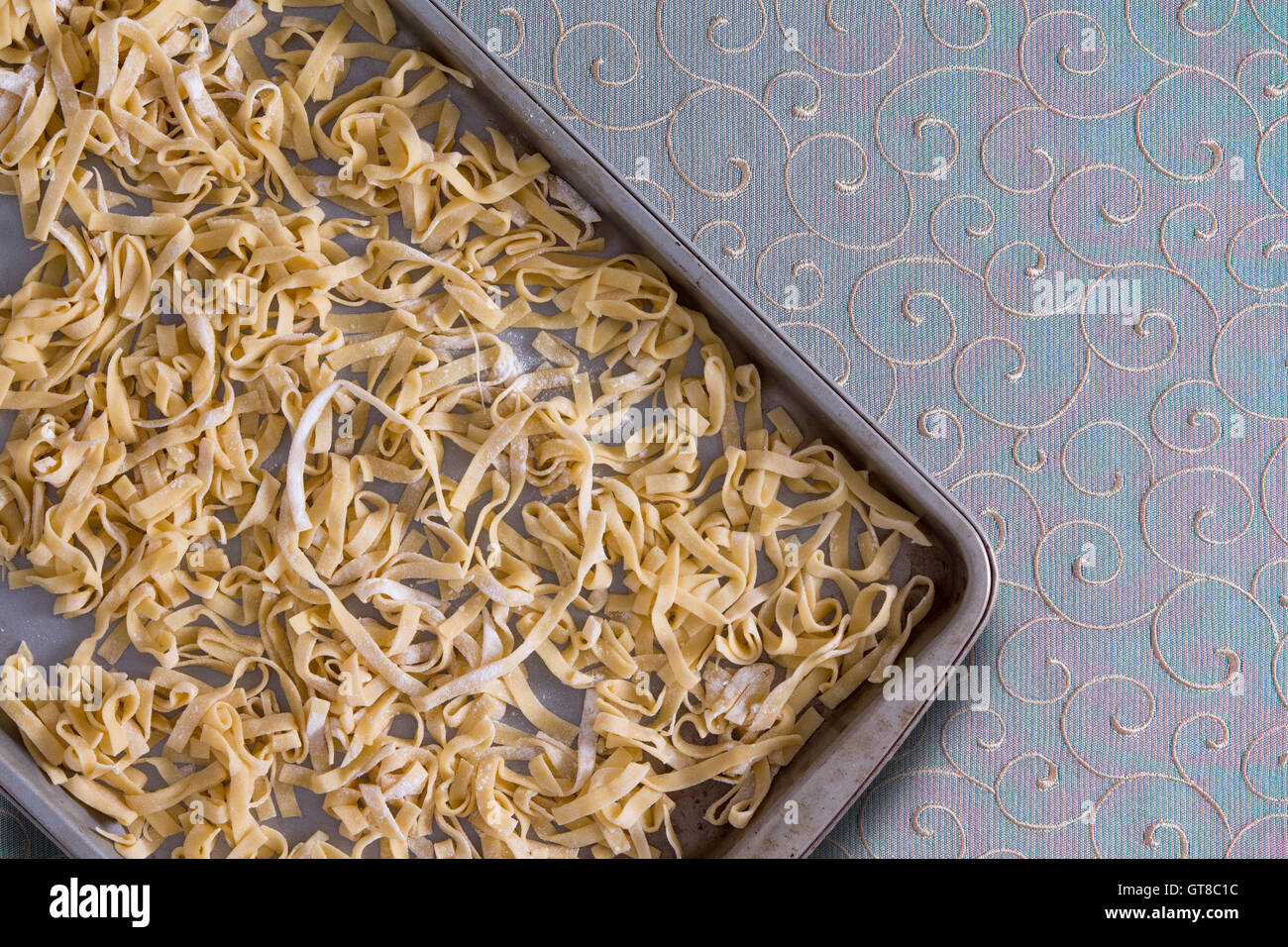 Vista aerea di freschi fatti in casa fettuccine tagliatelle essiccazione su un vassoio metallico posto su una tovaglia decorativa con moto vorticoso Foto Stock