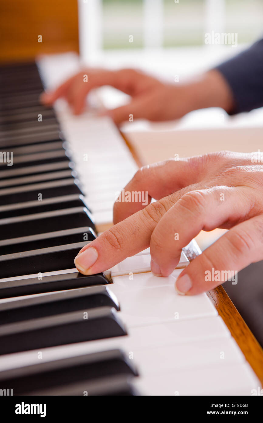 Uomo a suonare il piano con una vista ravvicinata delle sue mani sulla tastiera aperta come egli si estende per una nota Foto Stock