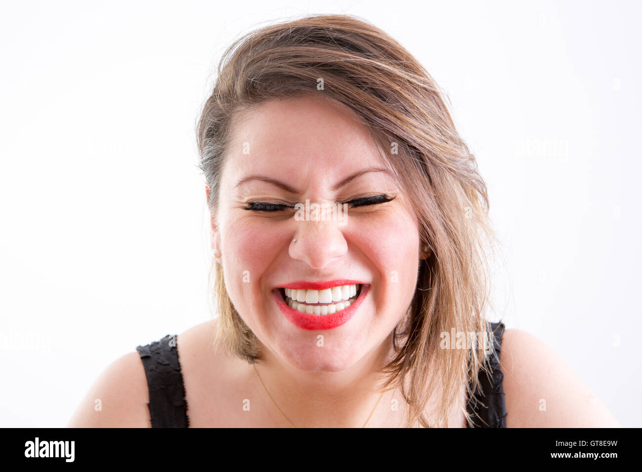 Vicino il volto di una donna bionda in Toothy ridere con gli occhi chiusi, di fronte alla telecamera, su uno sfondo bianco. Foto Stock