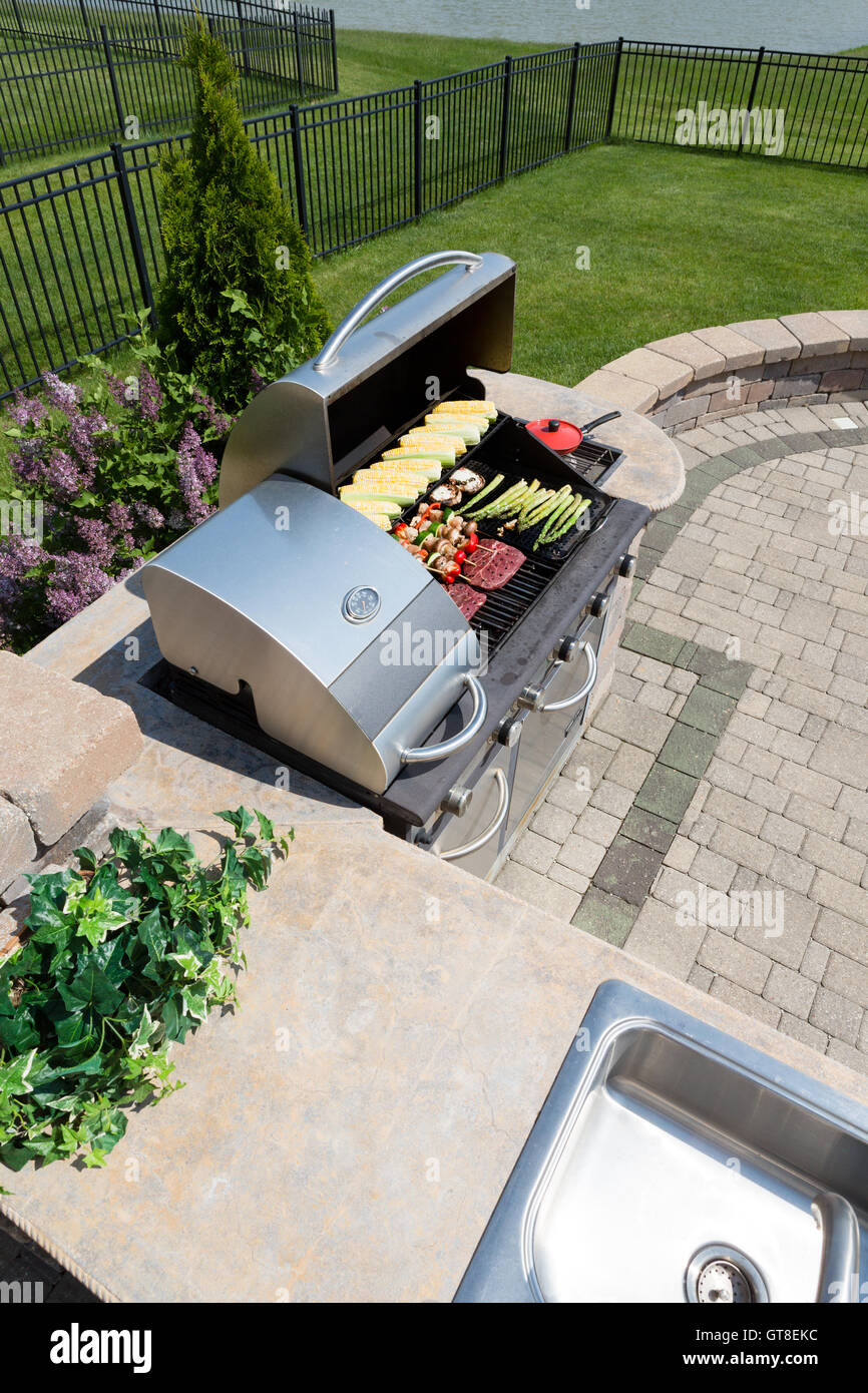 Una sana vita all'aperto una cottura in cucina estiva dotata di un lavandino e il contatore e grandi barbecue a gas caricato con veget fresco Foto Stock