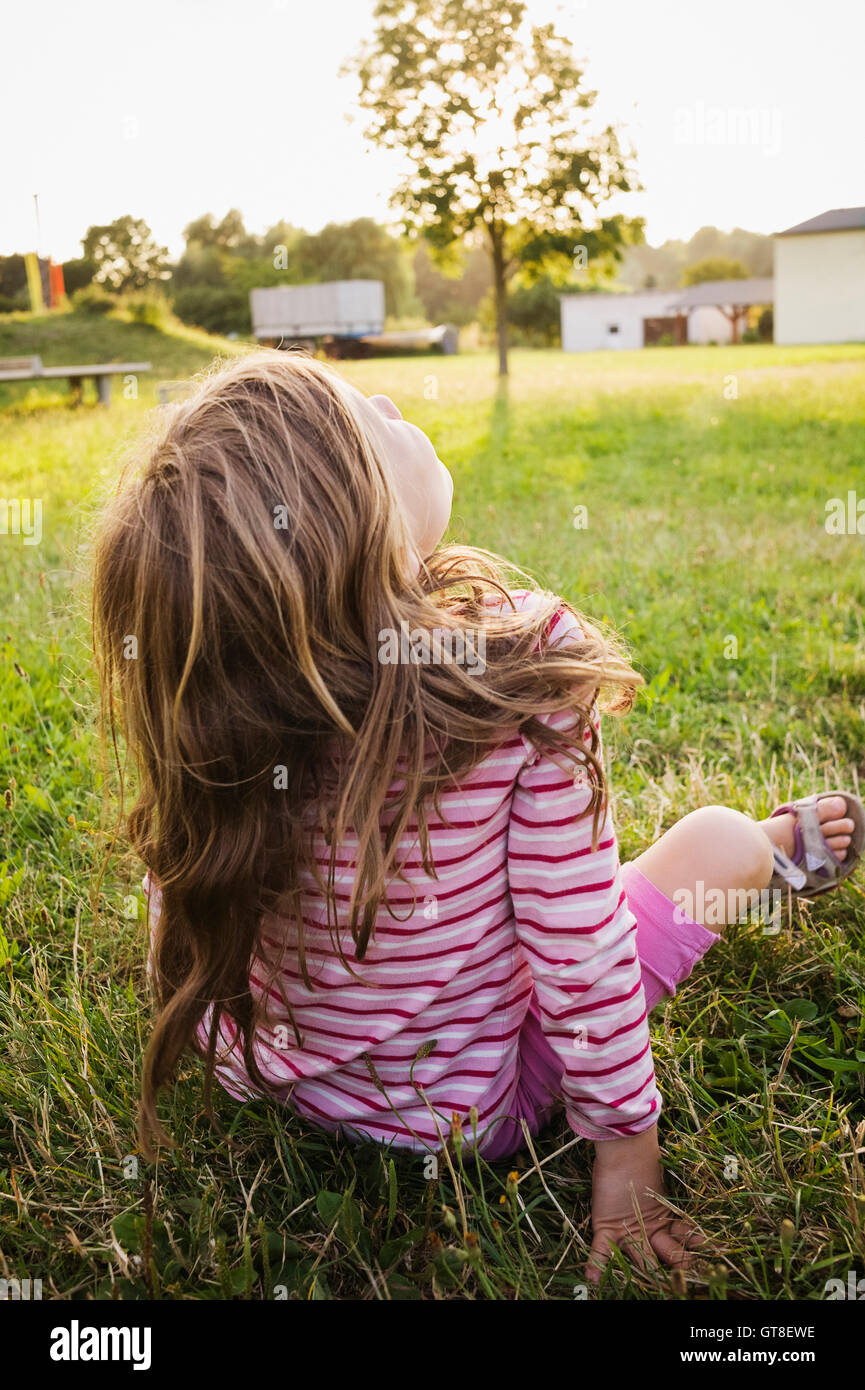 5 anno vecchia ragazza seduta sull'erba su un soleggiato sera e fissando il cielo, Germania Foto Stock