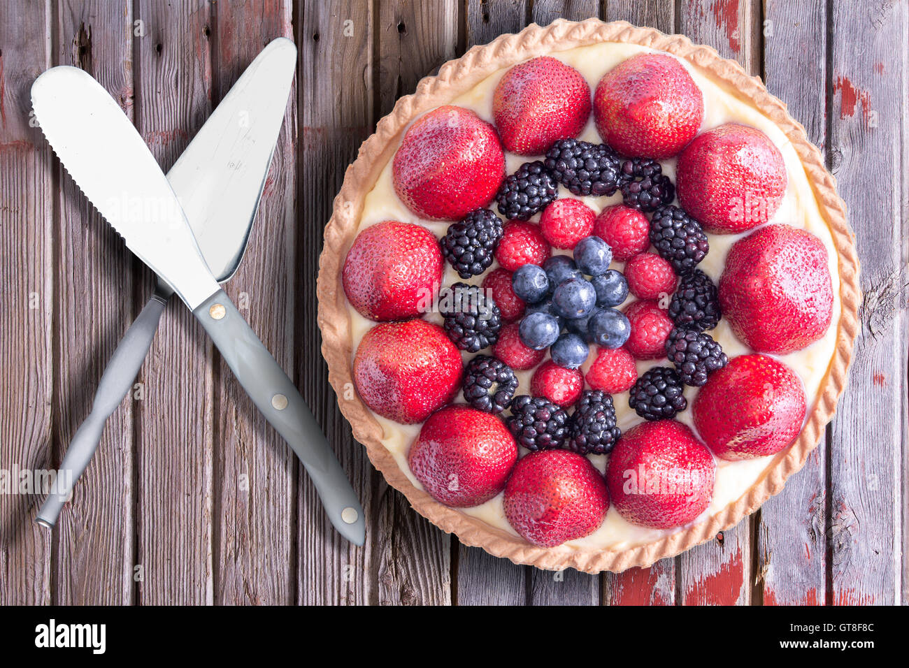 Frutti di bosco freschi fatti in casa crostata con servire utensili, posto su una tavola in legno rustico. Vista sopra. Foto Stock