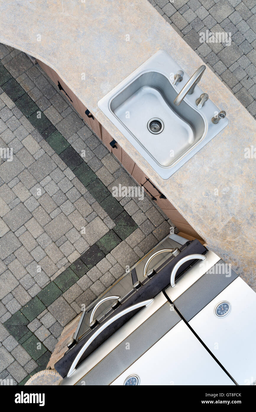 Sistemazione di cucina esterna e grande costruito in barbecue a gas in un design ad angolo con un cemento decorativo bancone e lavandino, overh Foto Stock