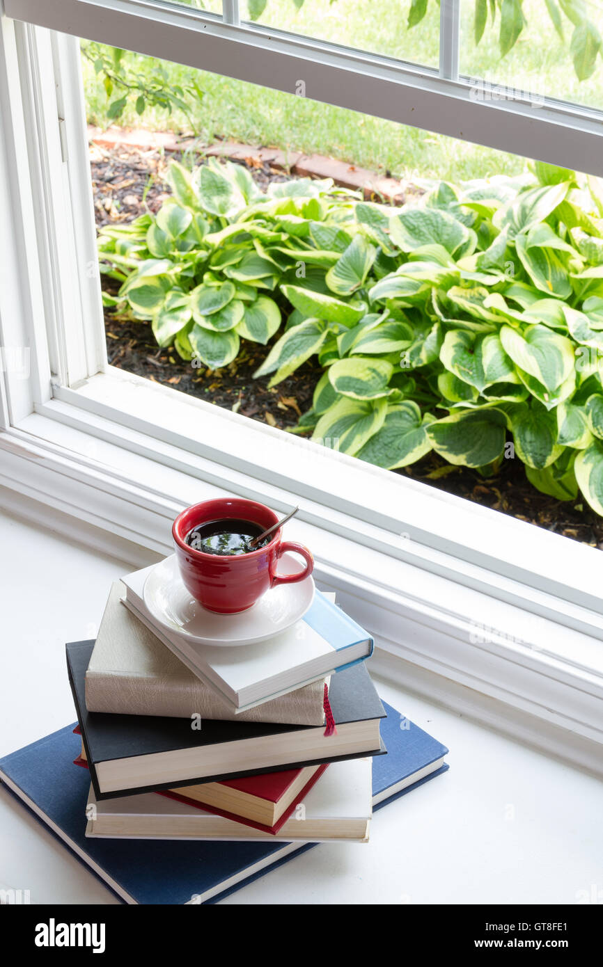 Lettura del concetto di tempo - a tazza calda di caffè nero sulla parte superiore dei Libri impilati alla finestra aperta vicino a Hosta piante. Foto Stock