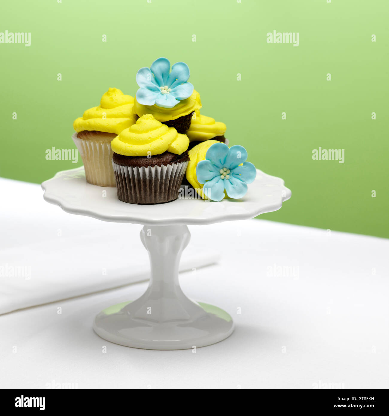 Cioccolato e vaniglia tortine con glassa di colore giallo e blu di fiori di zucchero su una torta di stand Foto Stock