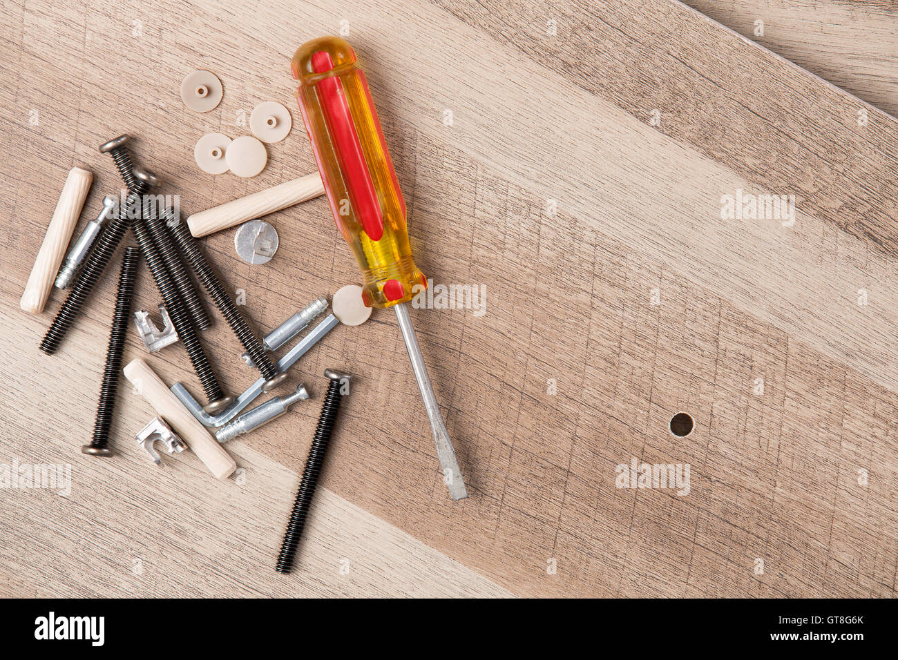 Angolo alto ancora vita vista di giallo gestite un cacciavite a lama piatta, viti e vari pezzi di Hardware accanto al piccolo foro Foto Stock