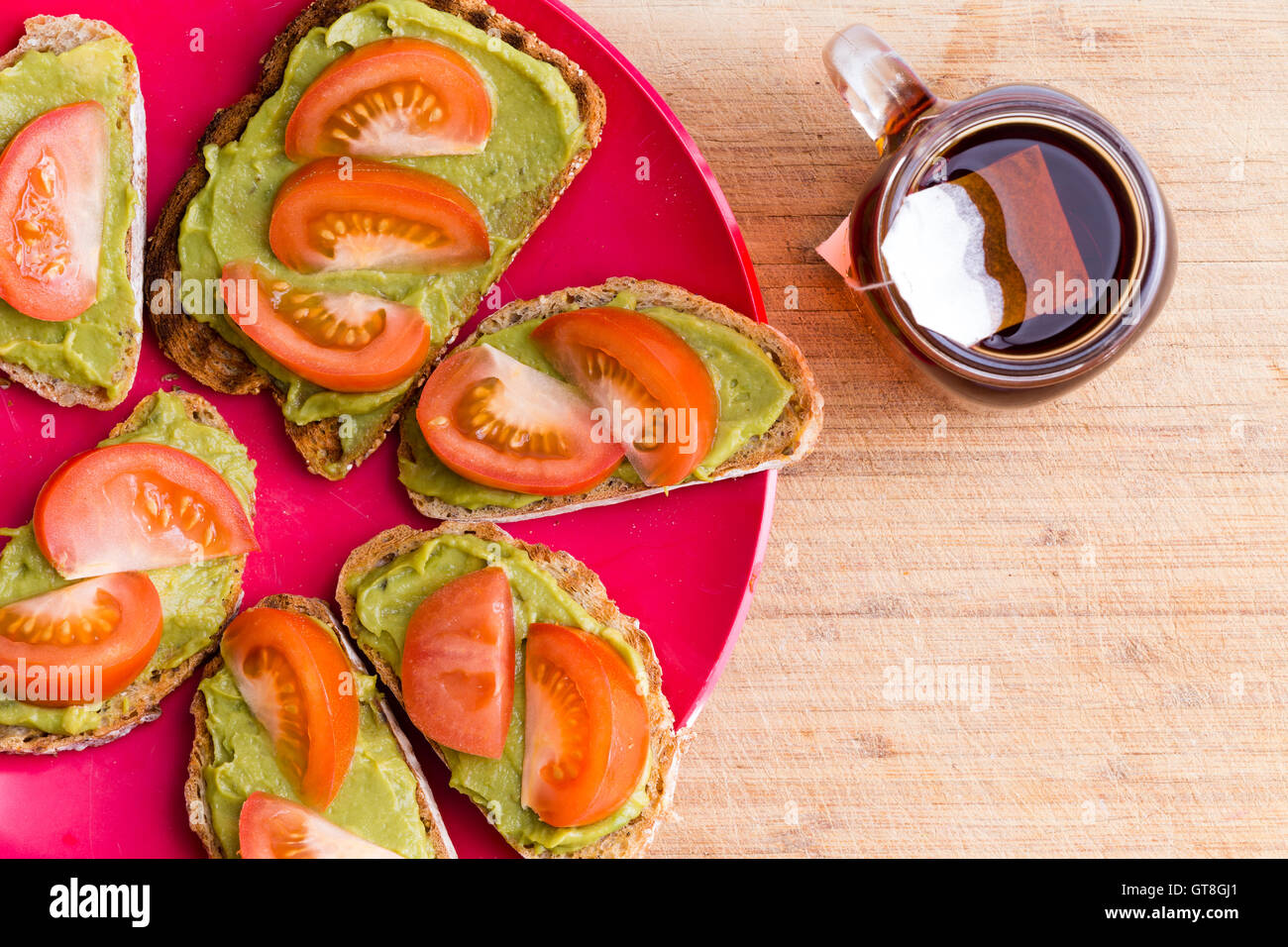 Vista dall'alto di avocado e pomodoro spalmato sul pane sulla targhetta rossa con la tazza di tè alle erbe Foto Stock
