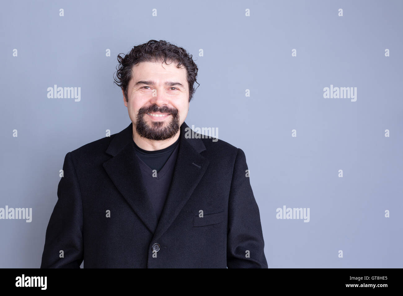 Unico sorridente bello dai capelli scuri e barbuto uomo di mezza età che indossa la maglia nera e blazer su sfondo grigio con copia sp Foto Stock