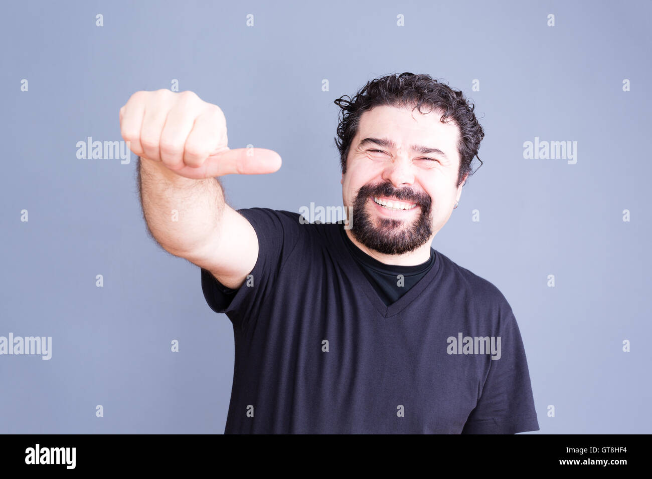 Vita Ritratto di gioiosa Laughing Man con la barba e capelli ricci dando pollice laterale lato gesto verso la telecamera in studio con Foto Stock