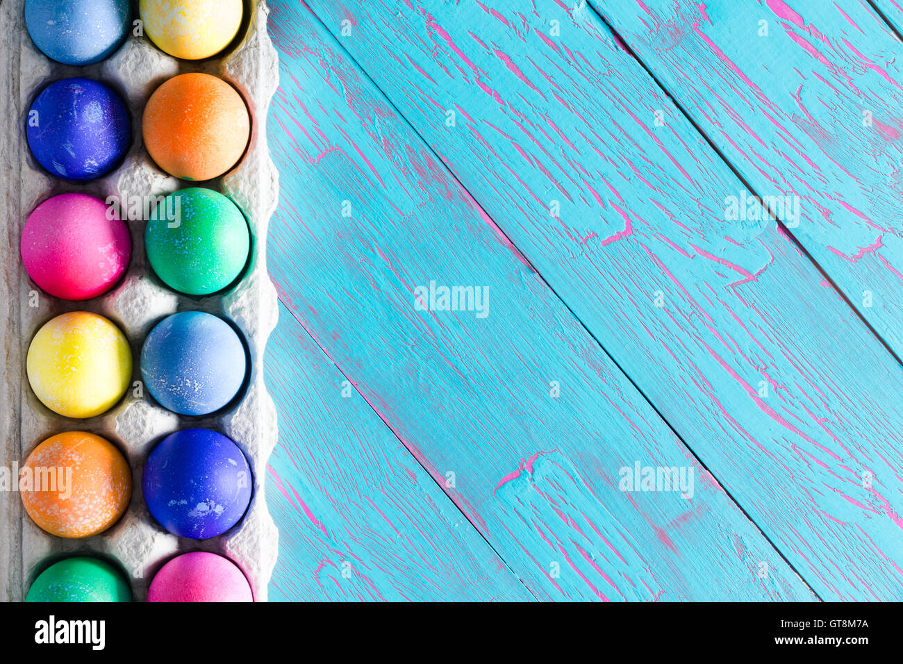 Pasqua Festa confine della mano uova tinti con i colori del arcobaleno disposti in un cartone uovo box su un tropicali colorati bl Foto Stock