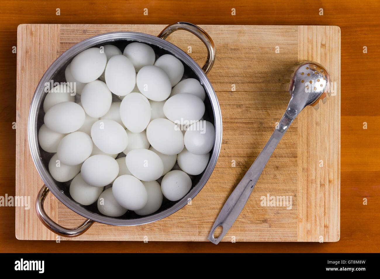 Bianco bollito uova di galline in una pentola di metallo o scolapasta in piedi su una tavola di legno di raffreddamento per decorare con colorante colorato per TH Foto Stock