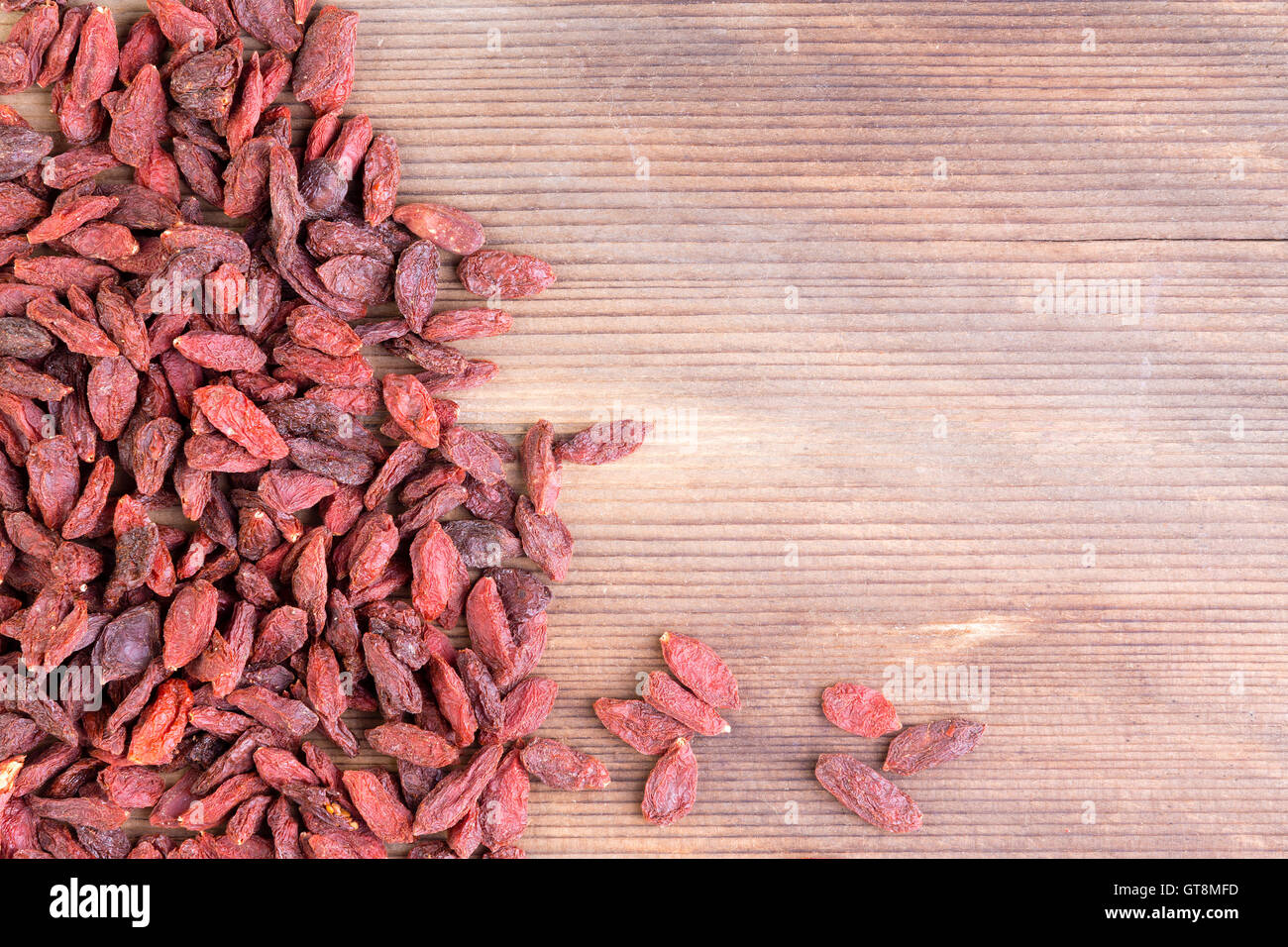 Pila di rossi secchi wolfberry cinese frutto spalmato su un lato del telaio con copia spazio su una superficie di legno Foto Stock