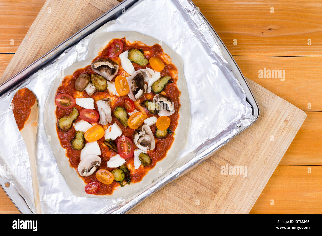 La mano si lancia in casa pizza vegetariana condito con pomodoro e un assortimento di verdure fresche, mozzarella e funghi ri Foto Stock