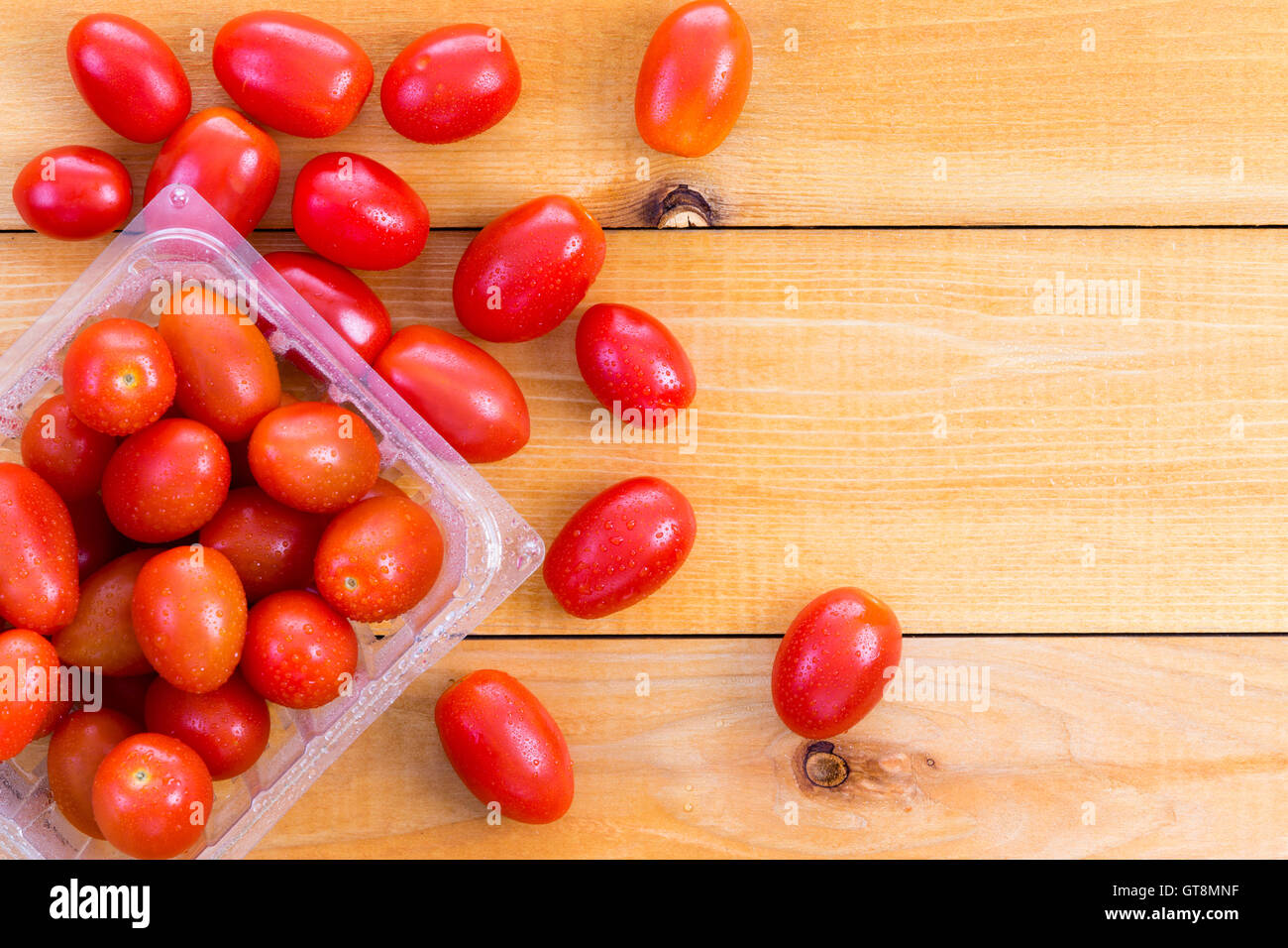 Cestella di fresco e salutare i pomodori baby visualizzato su una tavola di legno con alcuni sparsi intorno al fianco , copia spazio per lato Foto Stock