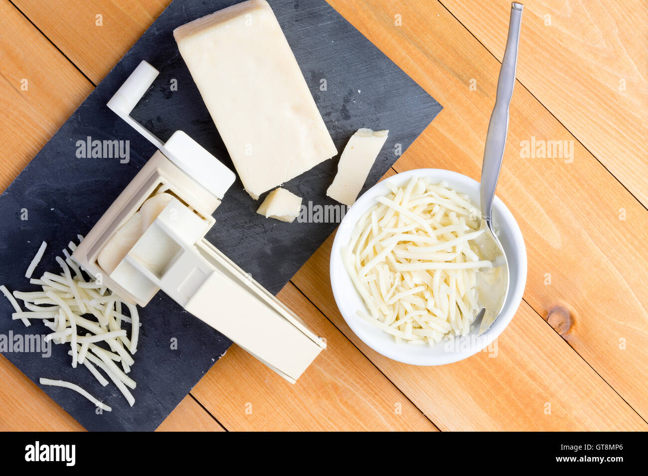 Preparazione grattugiate il formaggio gruviera per la cottura con una vista in pianta di una grattugia rotante e la fetta di formaggio su una scheda a fianco di gr Foto Stock