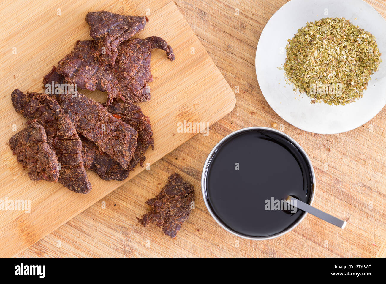 Rendere tradizionali fatti in casa a scatti di manzo o biltong con strisce sottili di carne di manzo magra carne su un tagliere al fianco di salsa teriyaki Foto Stock