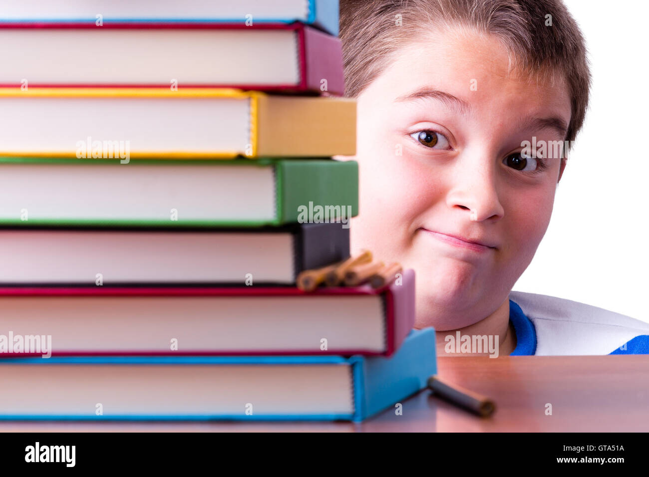 Cautamente ottimista giovane scolaro occhiatura fino ad alta pila di coloratissimi libri a copertina rigida con una bizzarra wide-eyed expressio Foto Stock