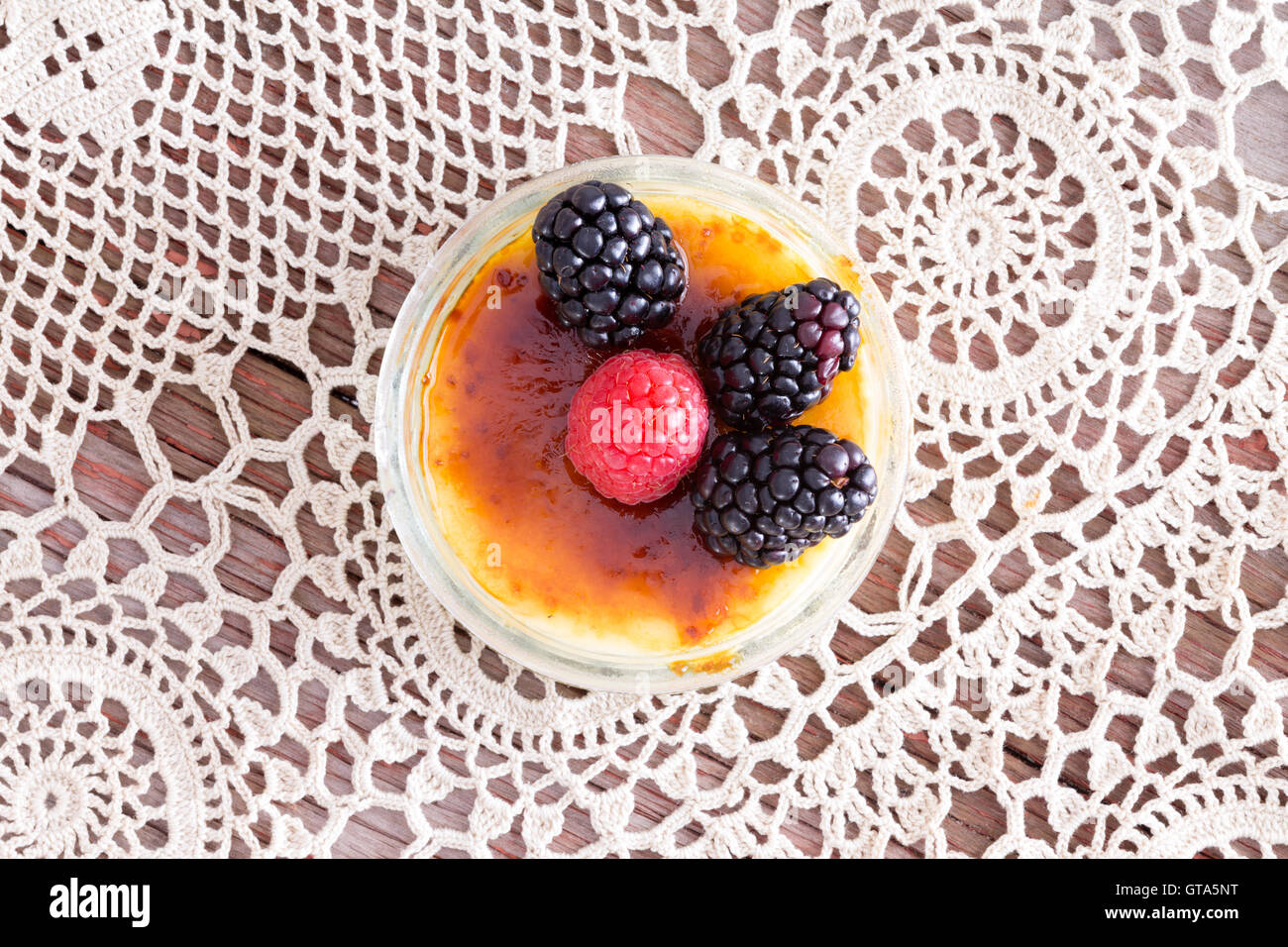 Preparate di fresco creme brulee con il rosso e il nero lamponi su vintage centrini. Foto Stock