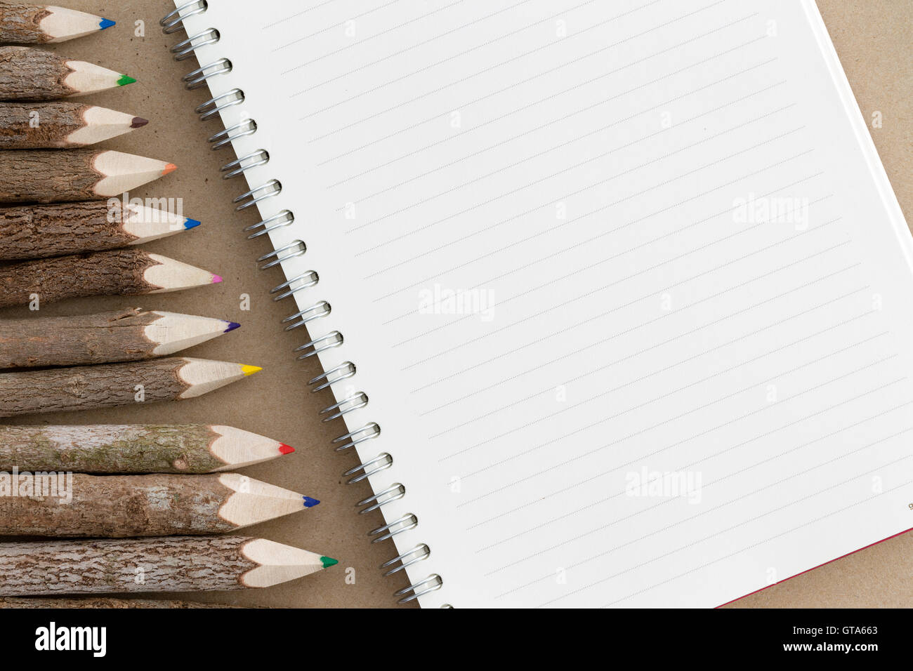 Rilegato a spirale notebook con un fustellato governata pagina con spazio copia accanto a un bordo angolato di rustico in legno naturale matita colorata Foto Stock