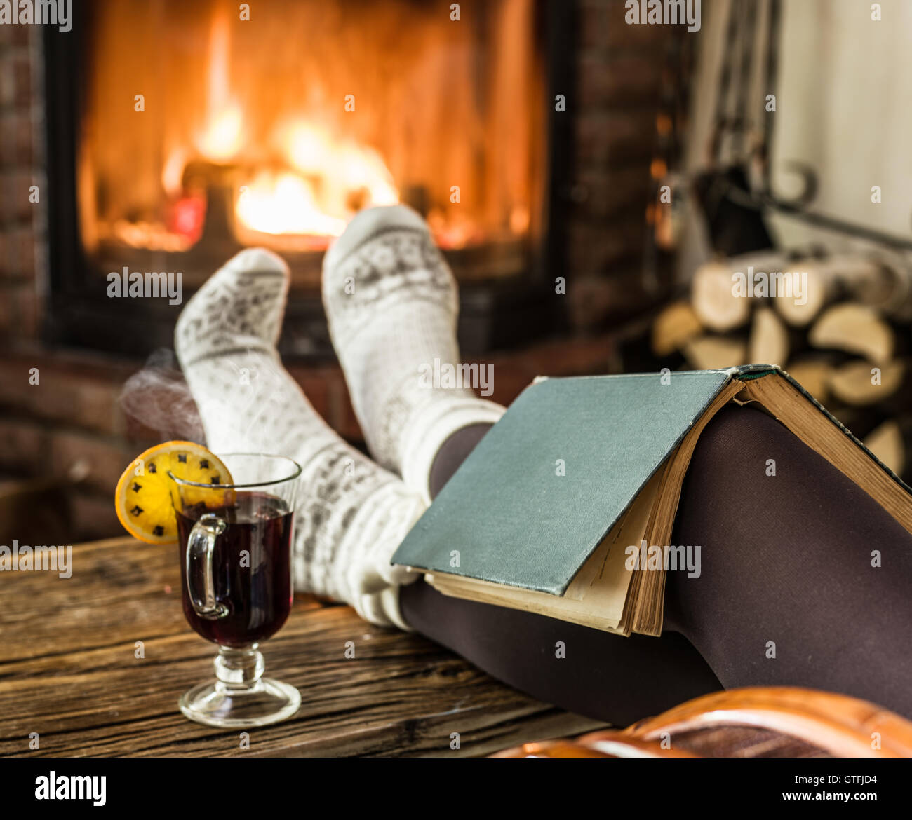 Vin brulé e prenota nelle mani della donna. Rilassarsi davanti al fuoco ardente nel freddo giorno d'inverno. Foto Stock