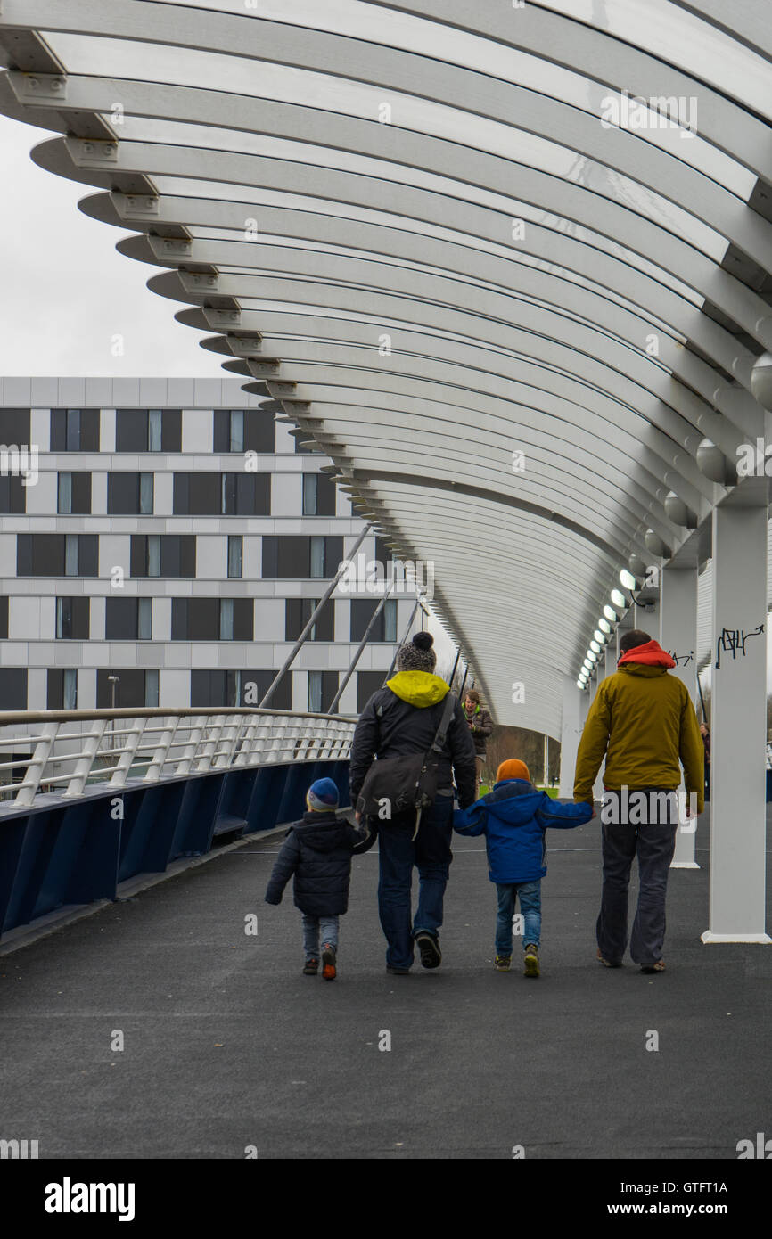 Camminando lungo un ponte a Glasgow 2 adulti tenendo le mani con 2 bambini. Appartamenti in background Foto Stock