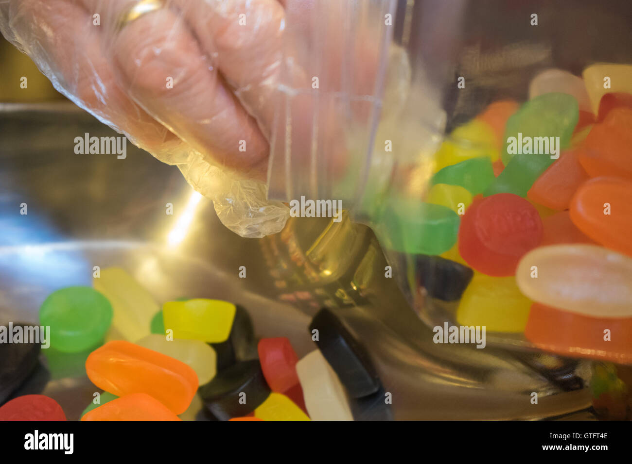 Misurazione di dolci (caramelle gommose, vivacemente colorato) da un vaso. Indossare dei guanti di plastica e una banda di nozze Foto Stock