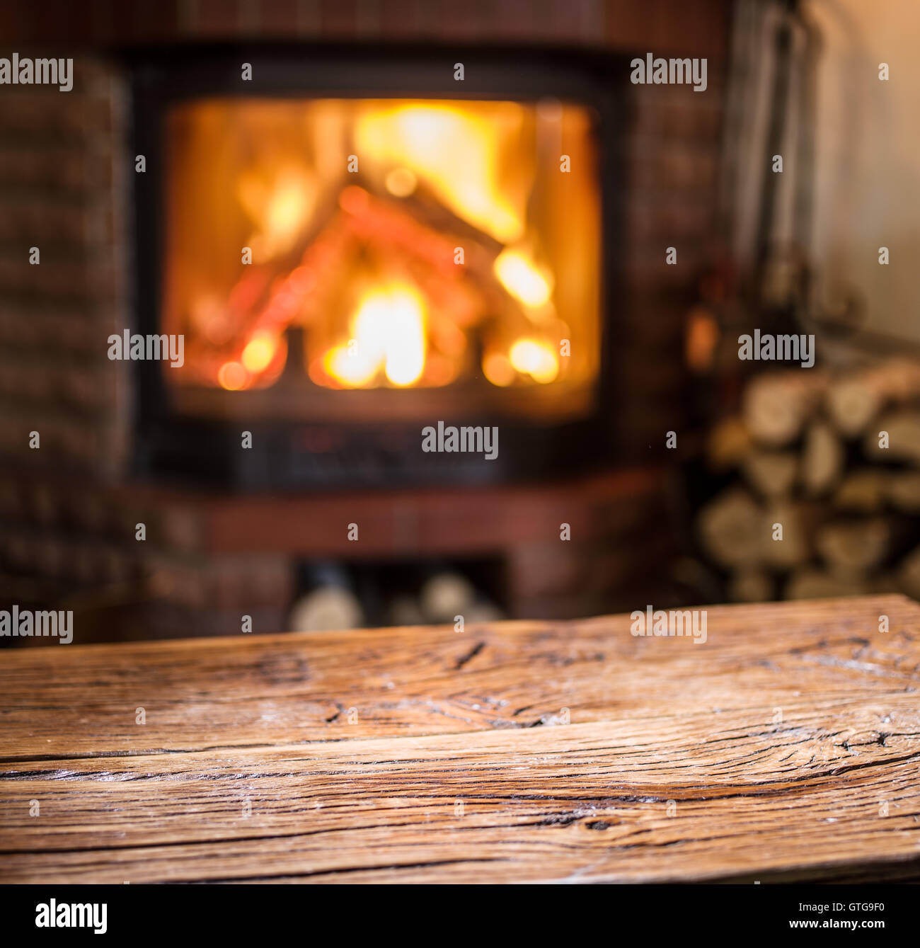 Vecchio tavolo in legno e camino con fuoco caldo sullo sfondo. Foto Stock