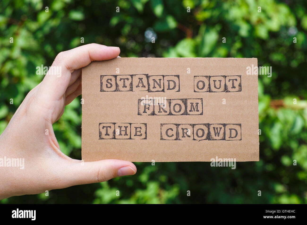 Donna mano azienda cartoncino con una frase Distinguiti dalla massa fatta da nero timbri alfabeto opposto sfondo verde Foto Stock