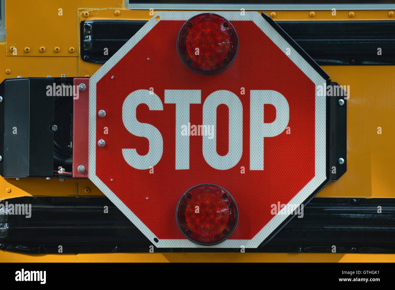 Un segnale di stop sul lato di un bus di scuola. Quando il bus si ferma per il carico o lo scarico agli studenti, il segno oscilla verso l'esterno per renderlo visibile. Foto Stock