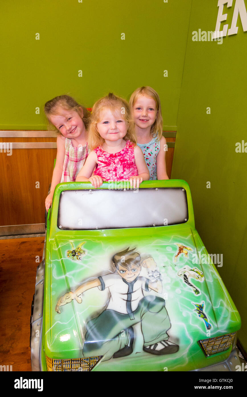 Tre ragazze di età compresa tra i 2 4 6 anni / giovani sorelle / bambini / Kids / ragazza godere a gettone bambino in auto in un centro commerciale per lo shopping arcade Foto Stock