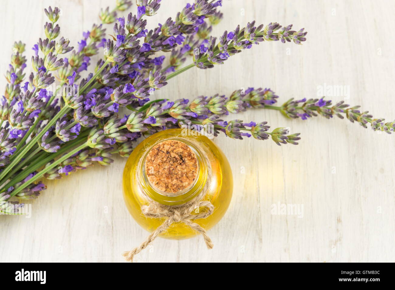 Olio di lavanda con fiori freschi di rami su una tavola di legno Foto Stock