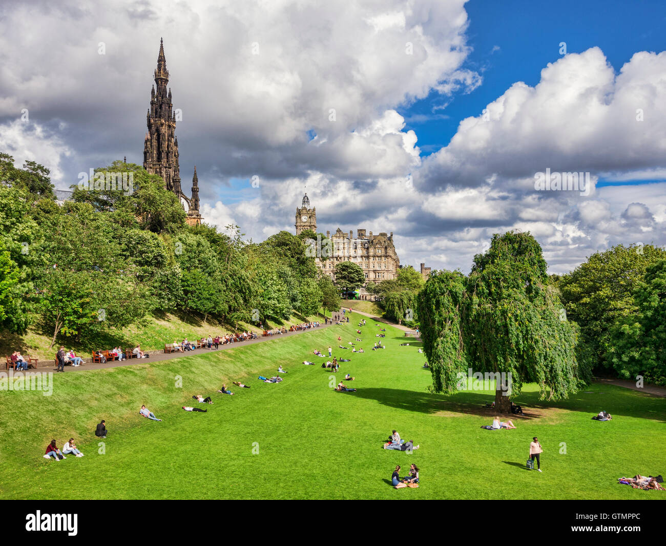 La gente a prendere il sole in Princes Street Gardens, Edimburgo, su di un bel giorno di inizio autunno con con il Monumento di Scott e il Balmoral Foto Stock