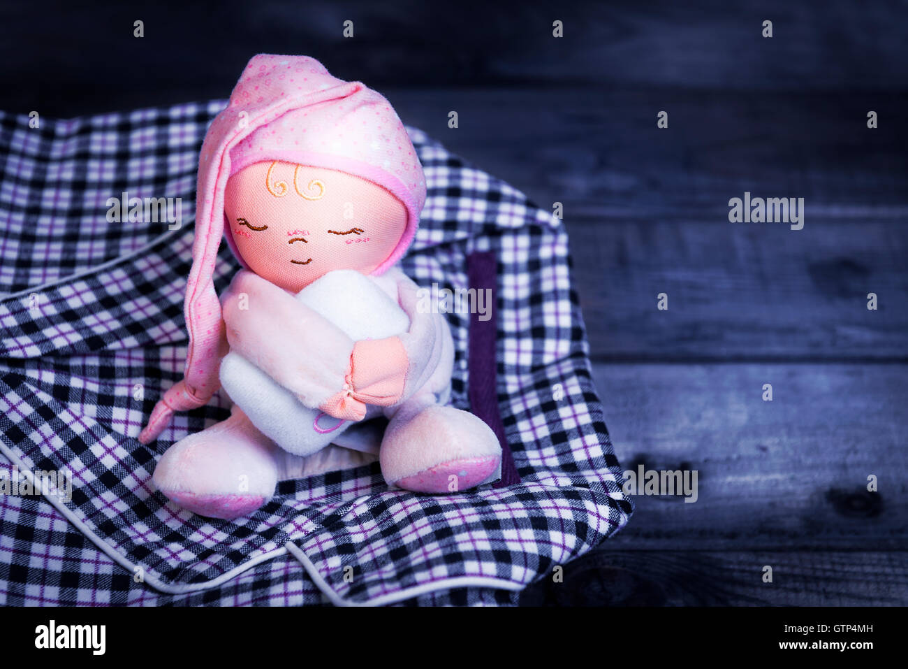 Su un tavolo di legno a scacchi pigiami di flanella e un soffice bambola giocattolo dormire uomo in un cappello rosa con un cuscino sotto le sue mani Foto Stock