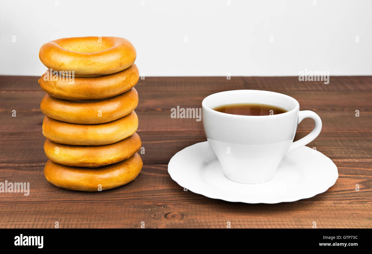 Mazzetto di deliziose rosy e bagel accanto a un bianco tazza di tè su un piattino giacciono su di un tavolo di legno Foto Stock